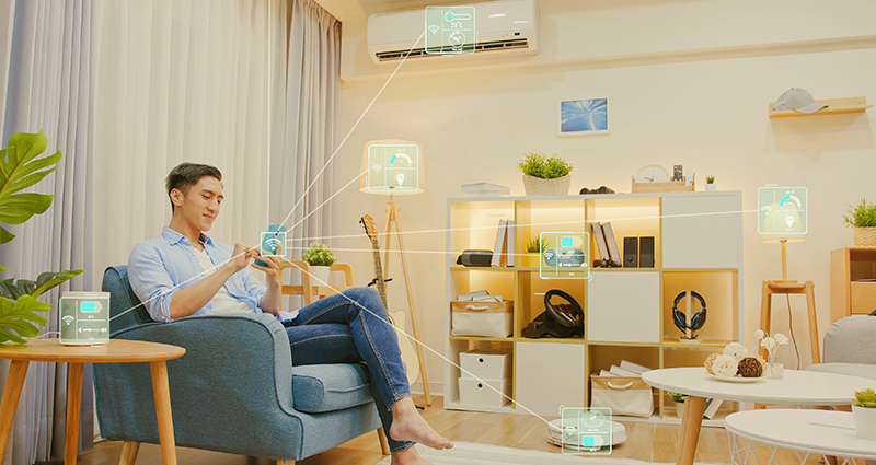 Guy sitting in a chair in his living room on mobile phone showcasing all of the devices he can access 