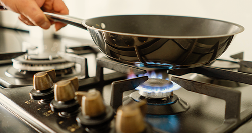 Person holding frying pan over stove flame
