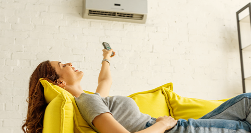 Woman on couch under portable air conditioner with remote in hand