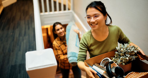 Two women is carrying a box of belongings as she walks up a flight of stairs