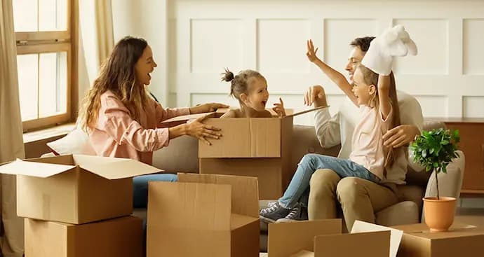 A family carries boxes into their new home, smiling and working together during the moving process.