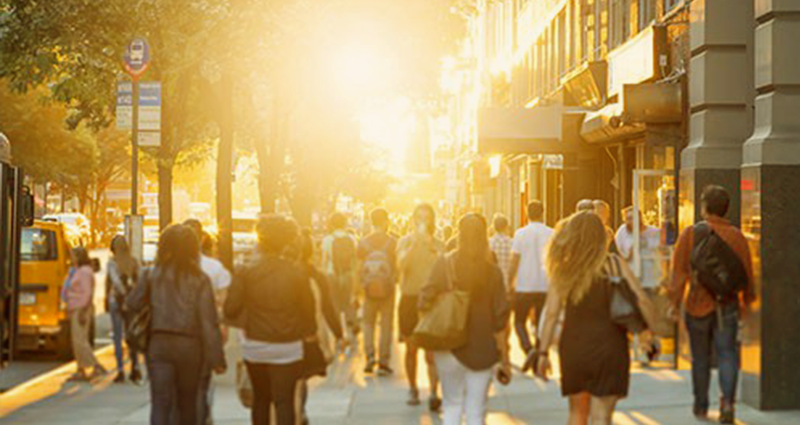 Busy city street with people walking and sun setting