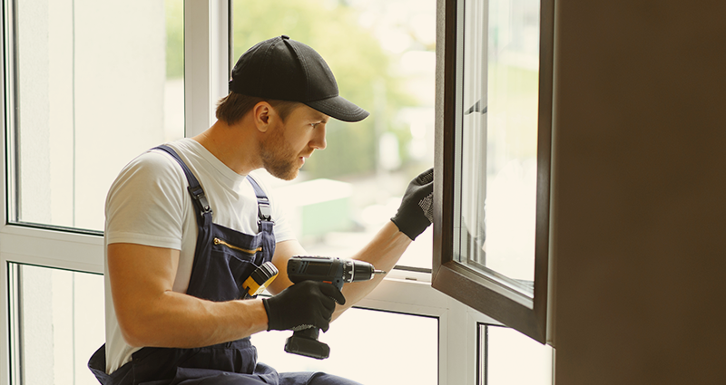 Contractor in overalls installing window with drill in hand
