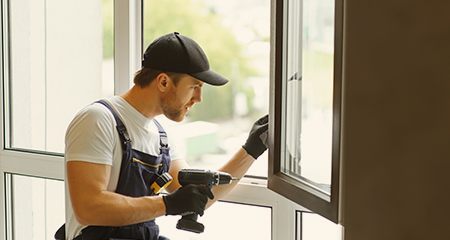 Contractor in overalls installing window with drill in hand