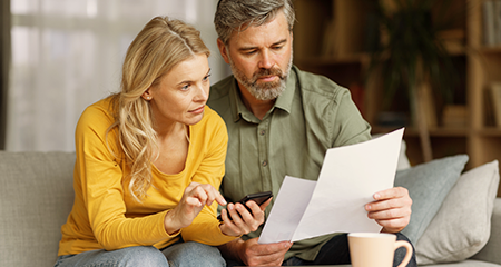 Couple sitting on couch looking at papers and female has calculator in hand