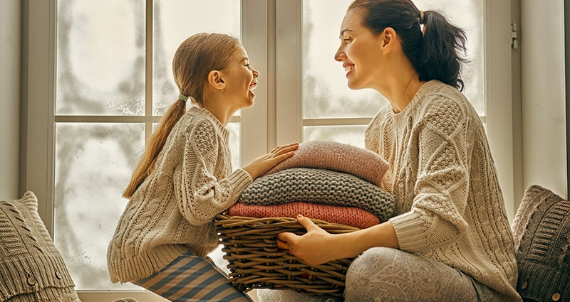 Mom and daughter with basket of blankets in front of window