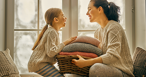 Mom and daughter with basket of blankets in front of window