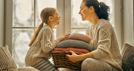 Mom and daughter with basket of blankets in front of window