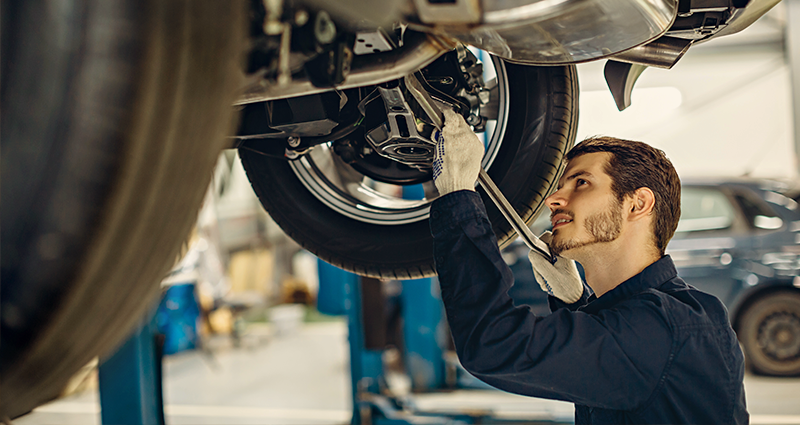 Male car mechanic working under vehicle with wrench in hand