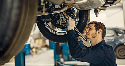 Male car mechanic working under vehicle with wrench in hand