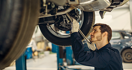 Male car mechanic working under vehicle with wrench in hand