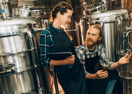 a man and woman standing together in front of a brewery, showcasing the building's entrance and outdoor seating area.