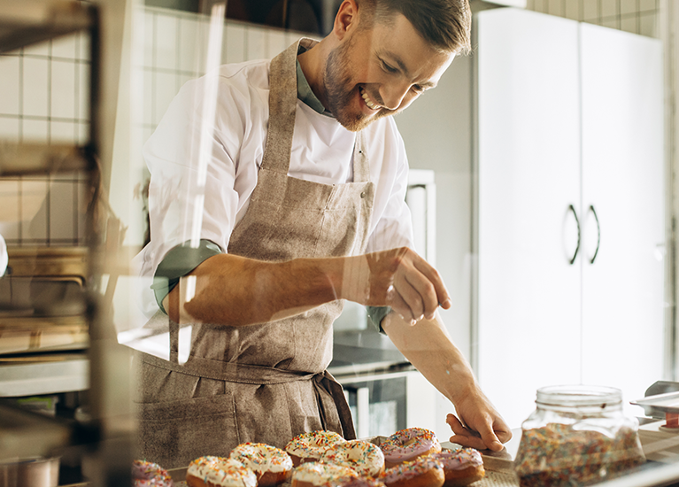 Baker sprinkling a topping on baked goods