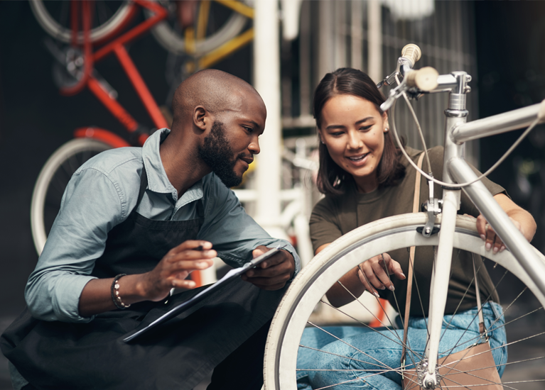 Technician  with clipboard and female customer looking over bicycle tire