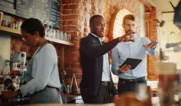 Three people in a restaurant, gathered around a tablet, reviewing table layout.